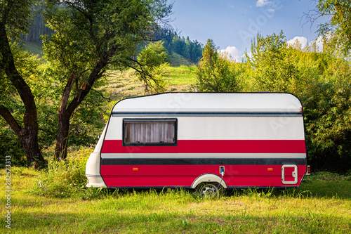 A car trailer, a motor home, painted in the national flag of Poland stands parked in a mountainous. The concept of road transport, trade, export and import between countries. Travel by car