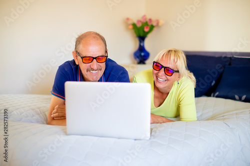 Foto Happy smiling senior couple looking at the screen of a laptop, wearing yellow-or