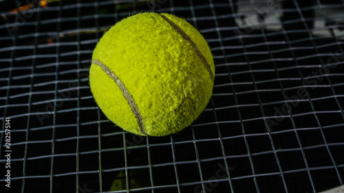close up of green tennis ball above black racket string isolated in black