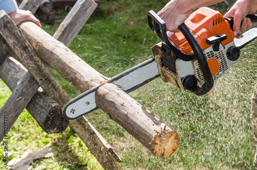 The employee produces a chainsaw sawing wood parts on a special device  outdoors  in the yard