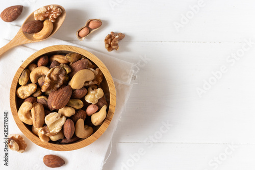 Top view of mixed nuts in a wooden bowl on white background