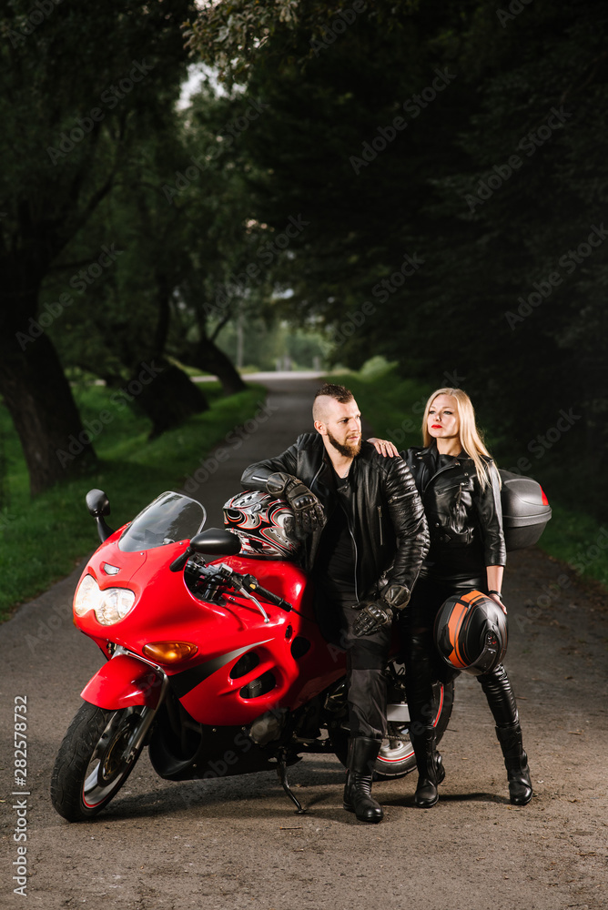 Obraz premium man and woman bikers in leather jackets with sports motor bike on the road in the evening