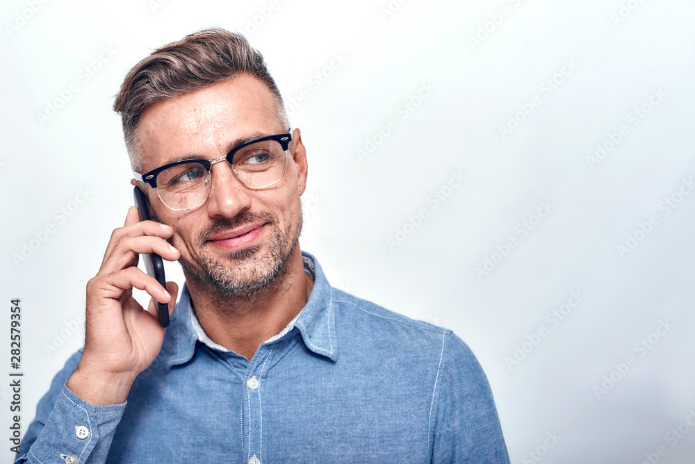 Glad to hear you Handsome and cheerful bearded man in casual wear talking on the phone and smiling while standing against grey background Glad to hear you Handsome and cheerful bearded man in casual wear talking on the phone and smiling while standing against grey background