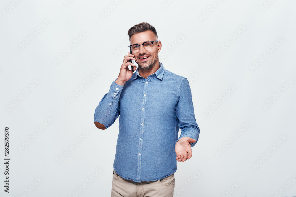 Great news Handsome and cheerful bearded man in casual wear talking on the phone and smiling while standing against grey background Great news Handsome and cheerful bearded man in casual wear talking on the phone and smiling while standing against grey background
