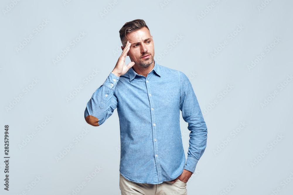 Lost in thoughts. Portrait of young and smart bearded man in casual wear touching his head and looking away while standing against grey background Lost in thoughts. Portrait of young and smart bearded man in casual wear touching his head and looking away while standing against grey background