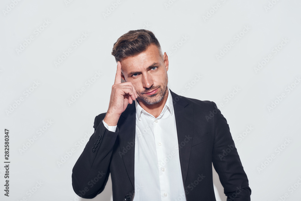 Time to think Confident bearded businessman touching his head by hand and looking at camera while standing against grey background Time to think Confident bearded businessman touching his head by hand and looking at camera while standing against grey background
