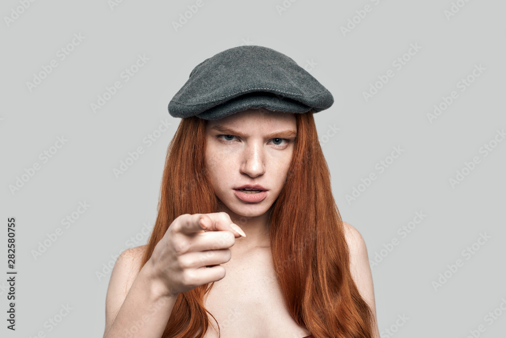I know everything about you. Portrait of young rude redhead woman in headgear looking at camera and gesturing while standing against grey background I know everything about you. Portrait of young rude redhead woman in headgear looking at camera and gesturing while standing against grey background