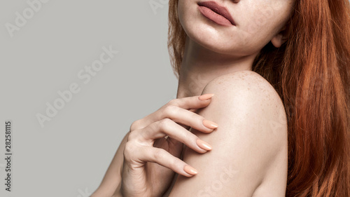 Tenderness. Beautiful young redhead woman touching her soft skin while standing against grey background photo