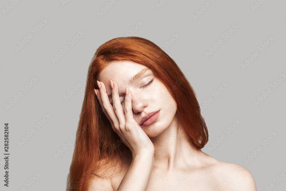 I am tired. Portrait of young frustrated teenage girl with long red hair keeping eyes closed and touching her face while standing against grey background I am tired. Portrait of young frustrated teenage girl with long red hair keeping eyes closed and touching her face while standing against grey background