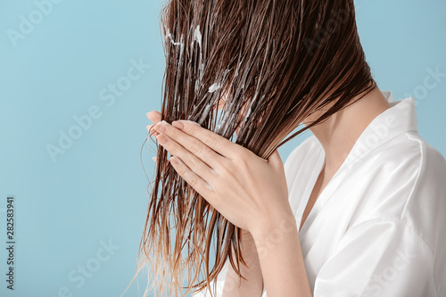 Beautiful young woman applying mousse on her hair after washing against color background