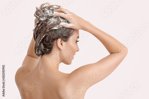 Beautiful young woman washing hair against light color background