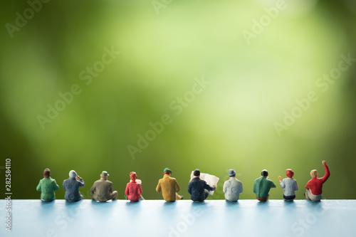 Miniature people, group of business people sitting on a book, doing activity and discussing ideas, society and teamwork concept.