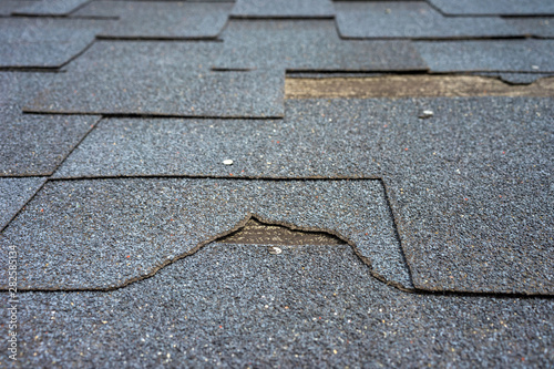 Close up view of bitumen shingles roof damage that needs repair.