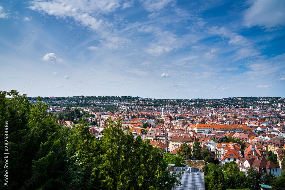 Germany, Summer sky over houses and roofs of stuttgart city in valley surrounded by trees and forest
