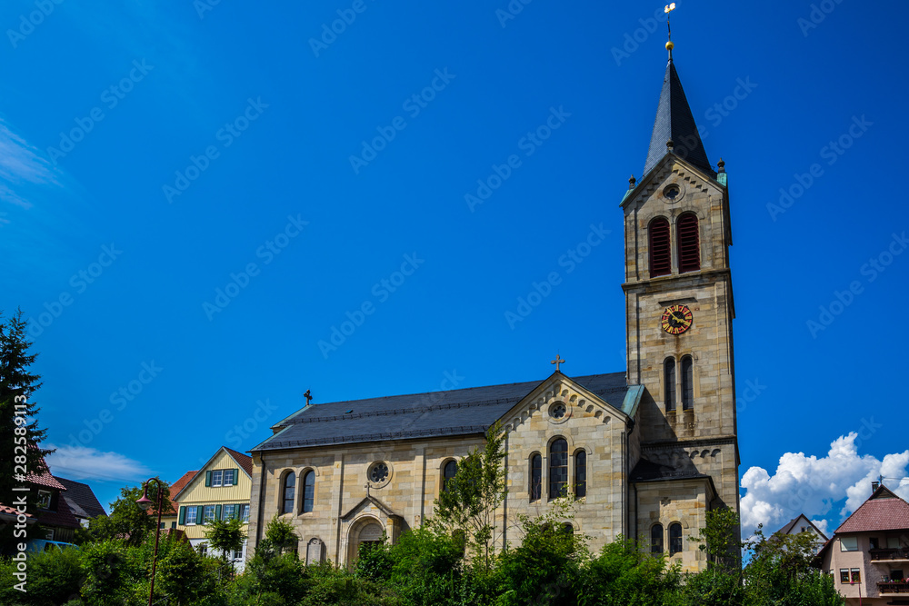 Germany, Beautiful ancient church building of kaisersbach near welzheim surrounded by green trees under blue sky