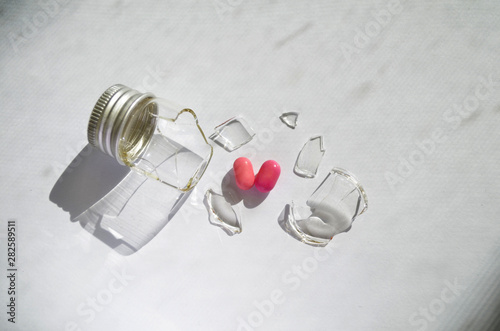 Photography A broken small glass bottle with metal cap, two pink heart-shaped tablets fell o