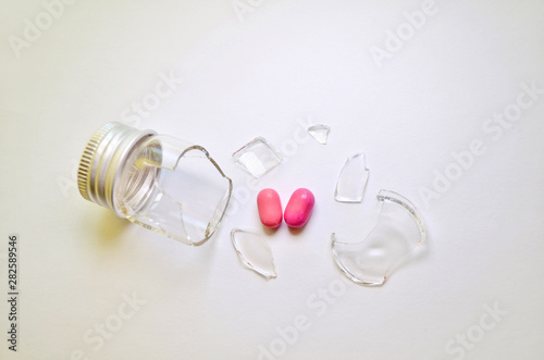 Canvas Print A broken glass bottle with a metal cap, two pink heart-shaped tablets fell out o