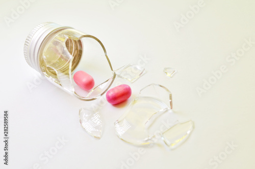 Canvas Print A broken small glass bottle with a metal cap, two pink tablets fell out of it, o