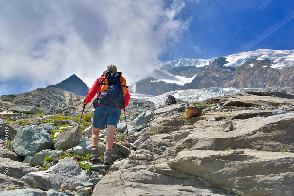 hiker climbing rocky mountain and heading for snow-capped summit of a glacier