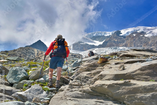 hiker climbing rocky mountain and heading for snow-capped summit of a glacier