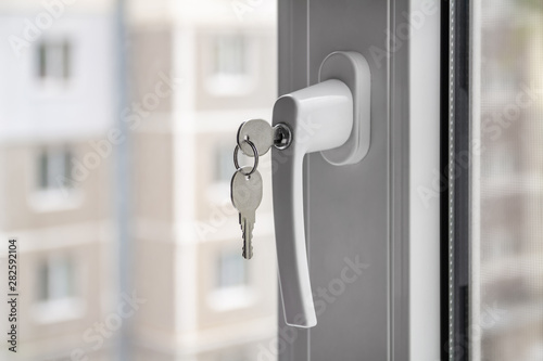 The concept of protecting a child from falling out of windows. Handle with a lock on the window. Apartment house on the background. Closeup, selective focus