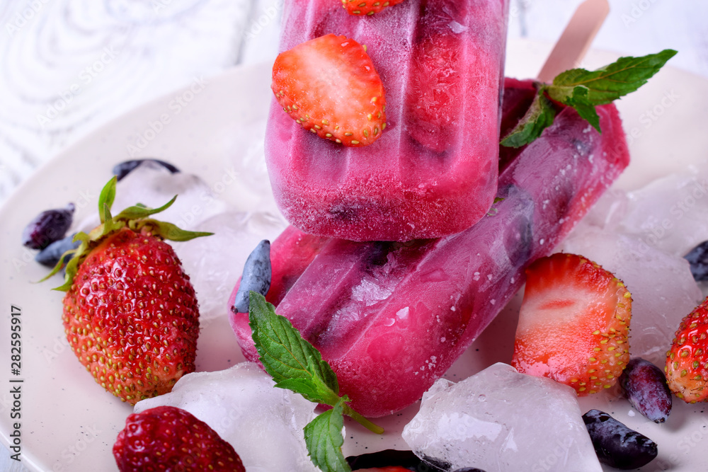 Berry popsicles with pieces of strawberry and honeysuckle on the white plate Berry popsicles with pieces of strawberry and honeysuckle on the white plate
