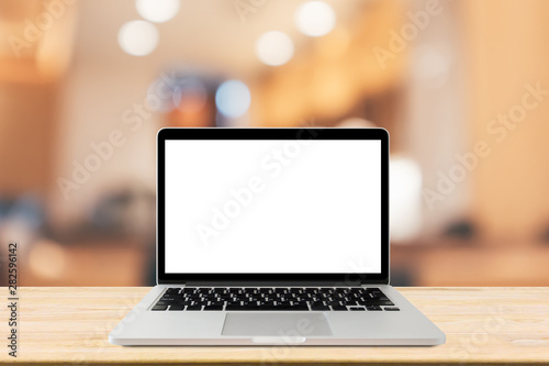 Blank screen laptop computer on wood table top with blur cafe restaurant with abstract bokeh light defocused background