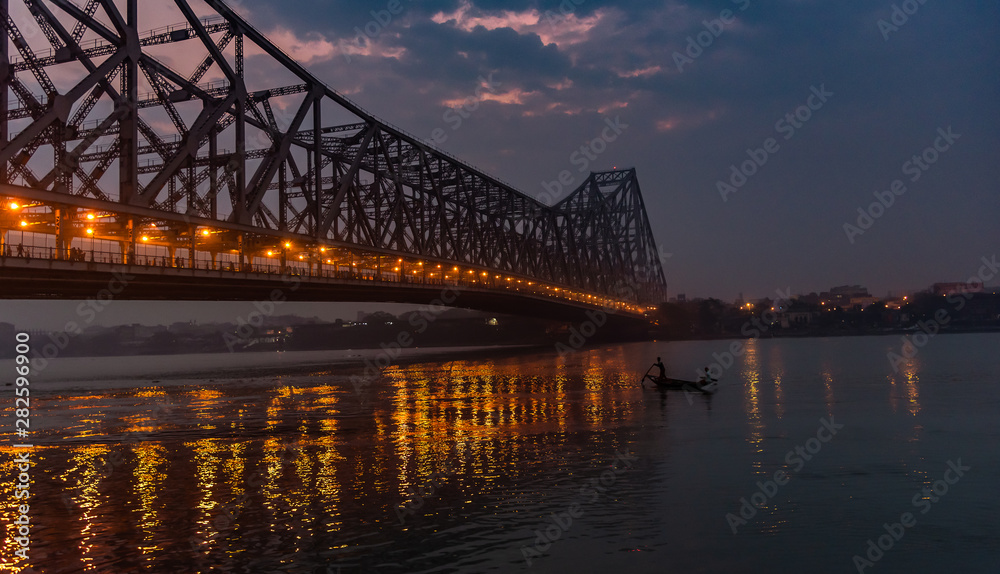 Silhouette of Howrah Bridge at the time of Sunrise.  Howrah Bridge is a bridge with a suspended span over the Hooghly River in West Bengal.