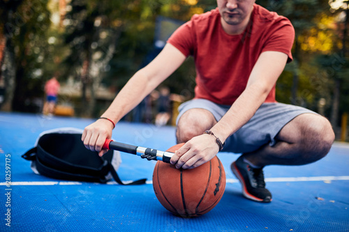 Foto Man inflating basketball ball with a hand pump on the urban court
