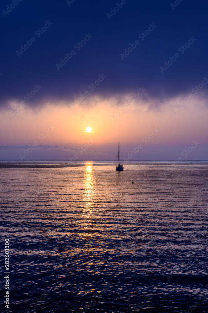 looking out into the mediteranean at sun rise with the reflection of the sun and a yacht