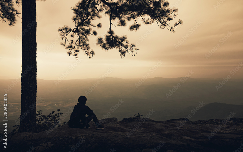 Silhouette of alone man sitting under big tree on the mountain view with fog in sunset background. Backpacker travel lifestyle and sad concept. Silhouette of alone man sitting under big tree on the mountain view with fog in sunset background. Backpacker travel lifestyle and sad concept.
