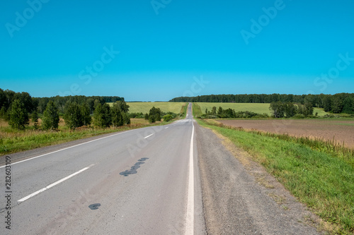 Fotografie The road through the meadows, perspectively stretching to the horizon, with a cloudy sky on a summer day
