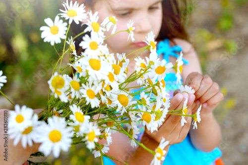 Sute kid girl holding a bouquet of daisies on a Sunny summer day. Mother's day. Family day. Concept of summer vacation.