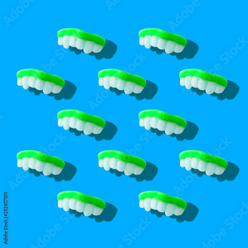 Photography collage of neon green color gummy milk teeth or jelly sweets on pastel blue background top view flat lay isometric pattern.Halloween holiday concept.surrealism,pop-art style.Square image
