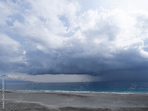 Distant rain and dramatic dark sky over sea with gravel beach in foreground