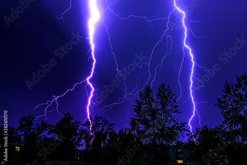 bright flashes of lightning during night thunderstorms, silhouettes of trees and houses against the dark blue sky