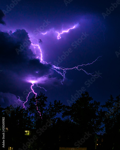 bright flashes of lightning during night thunderstorms, silhouettes of trees and houses against the dark blue sky