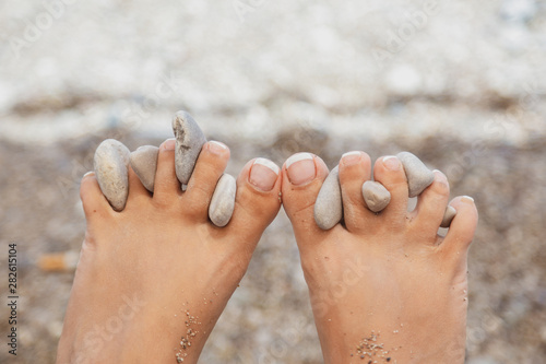 Canvas Print Closeup view of cute funny female legs with beach stones between toes