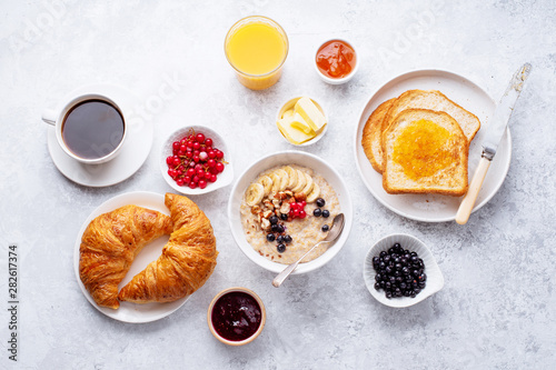 Breakfast with oatmeal with berries and nuts, croissants, toasts with jam and butter, coffee and orange juice