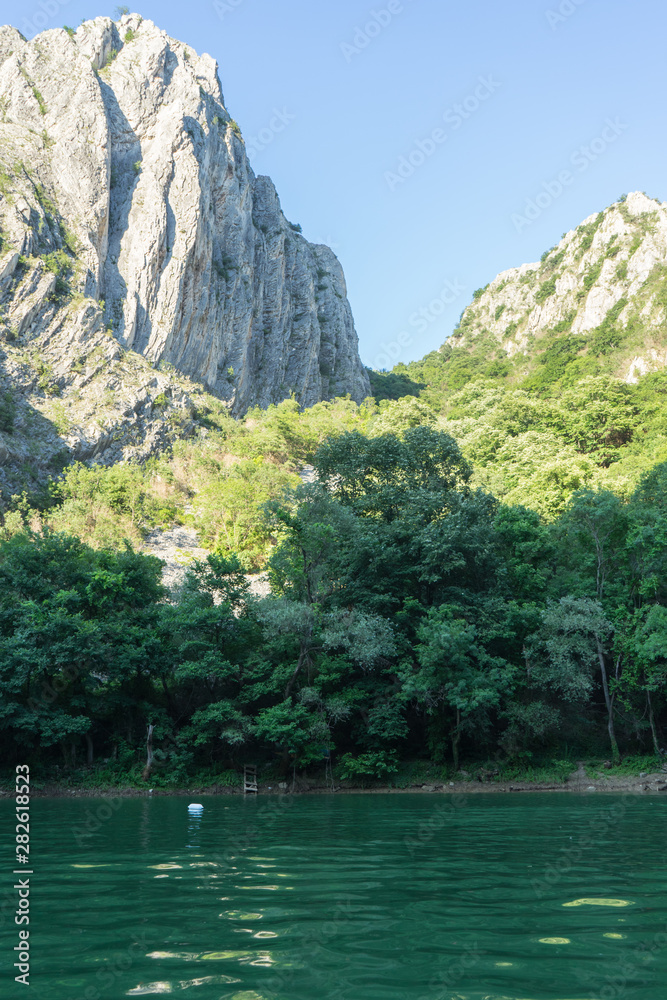 Scenic view with amazing mountains. Forest and river in Matka Canyon near Skopje in Macedonia. Vertical photography of the nature and great rock with sun