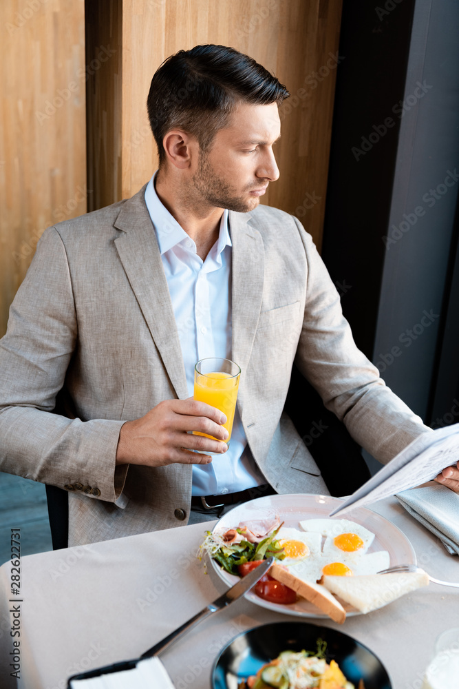 pensive businessman holding glass of orange juice and newspaper in cafe pensive businessman holding glass of orange juice and newspaper in cafe