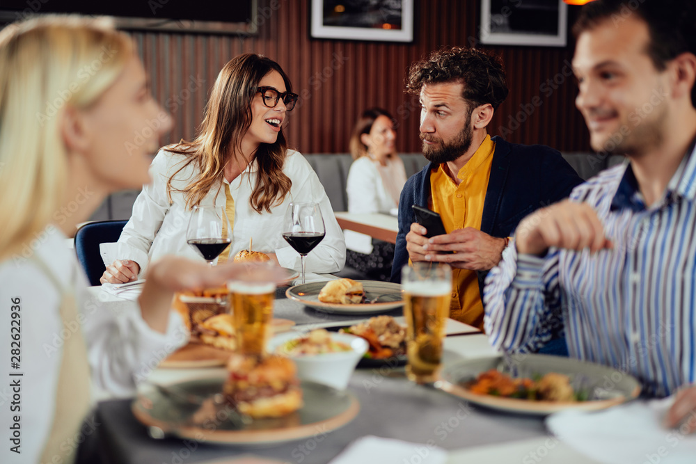 Multiethnic friends sitting at restaurant, drinking alcohol, chatting and having burgers for dinner.