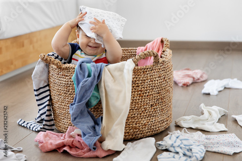 Funny baby sitting in laundry basket with clothes on head
