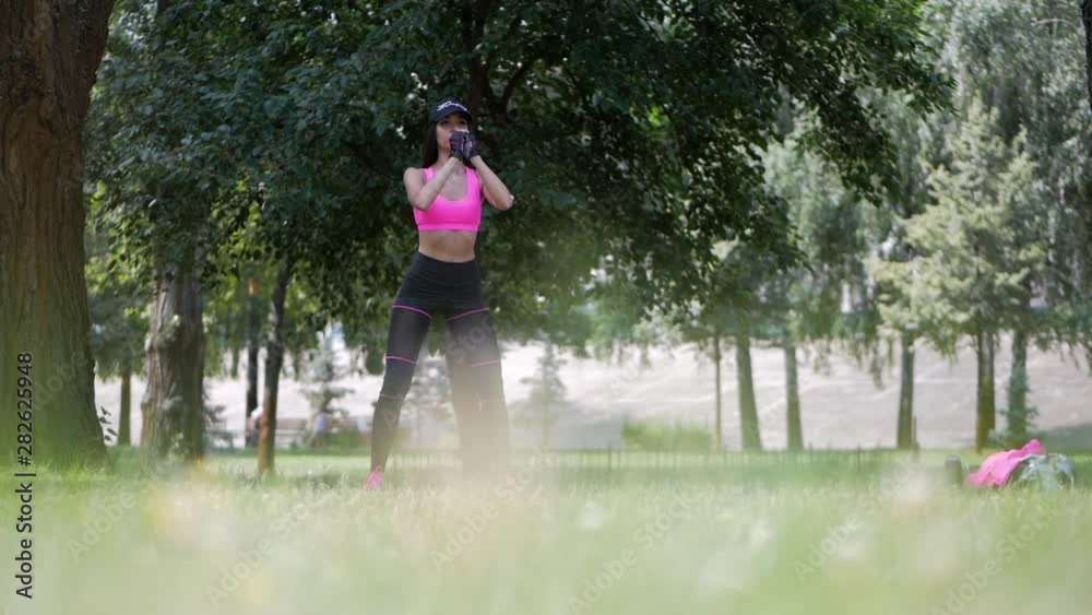 Smiling woman training squat exercise in city park. Attractive girl doing warm up exercise before fitness training outdoor. Fitness workout in green park Smiling woman training squat exercise in city park. Attractive girl doing warm up exercise before fitness training outdoor. Fitness workout in green park
