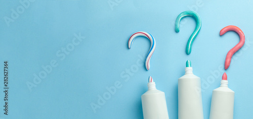 Question mark from toothpaste. Concept of choosing good toothpaste for teeth whitening. Tube of colored toothpaste on blue background. Copy space for text. photo
