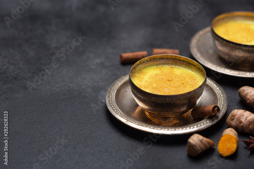 Golden turmeric milk on the black background with ingredients