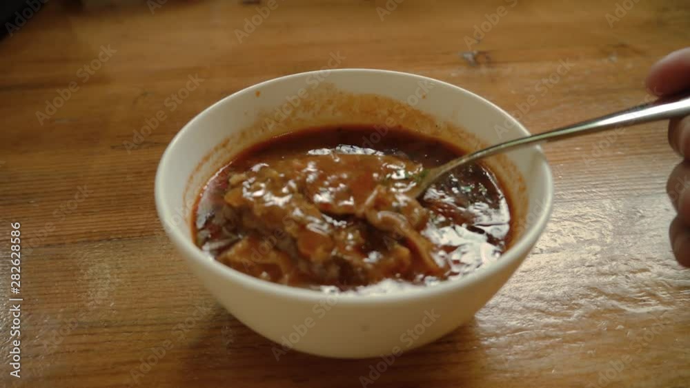 A bowl of hot Georgian kharcho soup with meat in a restaurant. man stirs lamb chunks in soup with a spoon.