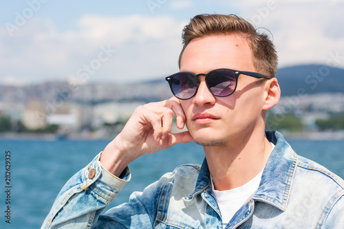 A young handsome man in sunglasses at the seascape background © allai