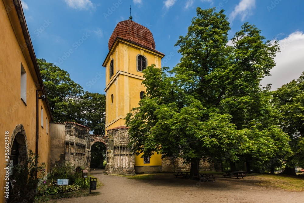 Panensky Tynec, Czech Republic - July 15 2019: Yellow bell tower and stone gateway, as a part of the unfinished Gothic church of the Virgin Mary from 14th century. Sunny summer day with blue sky.