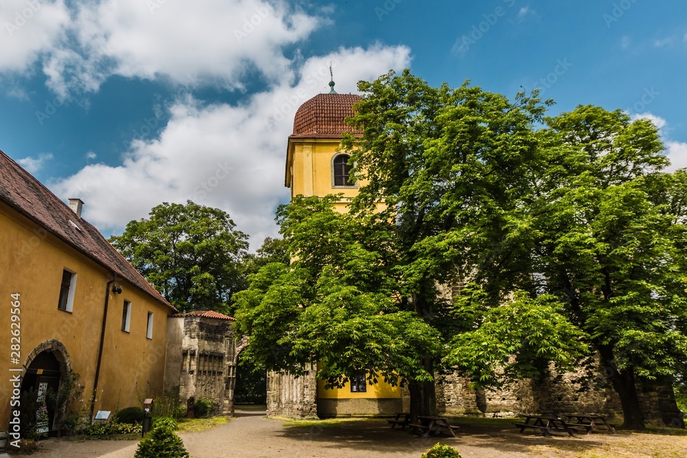 Panensky Tynec, Czech Republic - July 15 2019: Yellow bell tower and stone gateway, as a part of the unfinished Gothic church of the Virgin Mary from 14th century. Sunny summer day with blue sky.